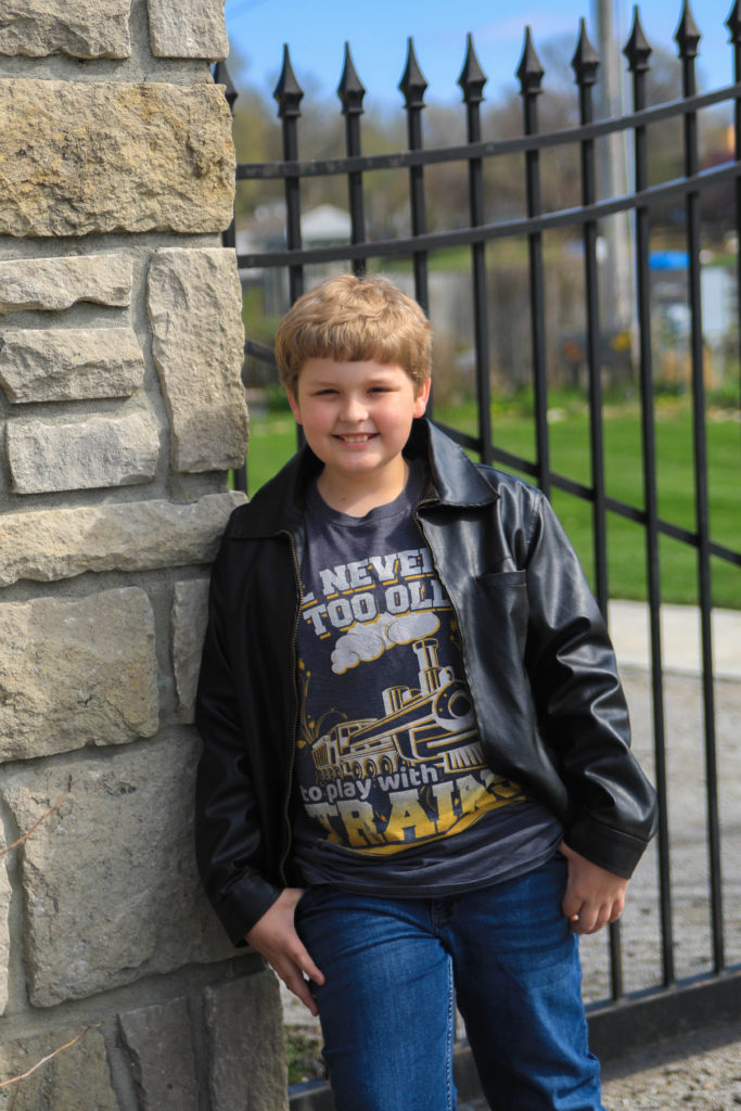 braden in train shirt lending on stone gate wall with jacket
