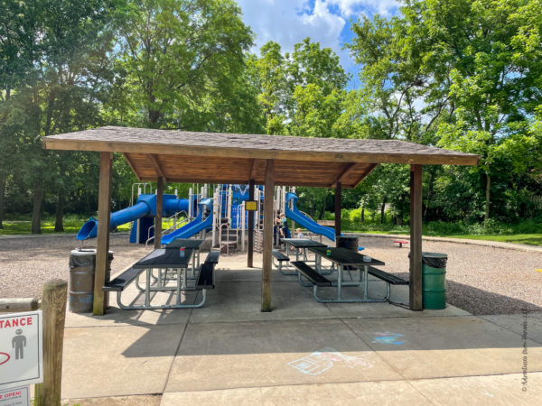shelter house with picnic tables in front of playground at park