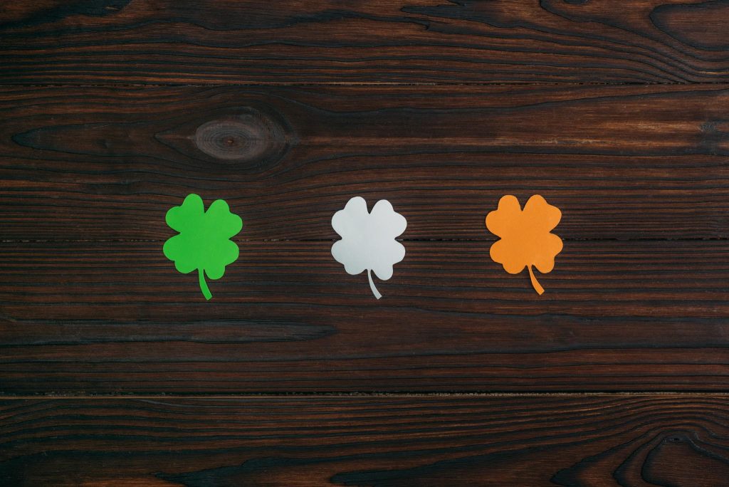 dark wood background, with a green shamrock, white shamrock, and orange shamrock laying in a line like the Irish flag
