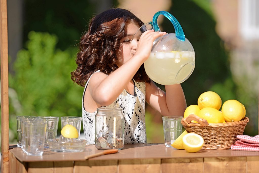 little girl drinking lemonade from a pitcher at a lemonade stand