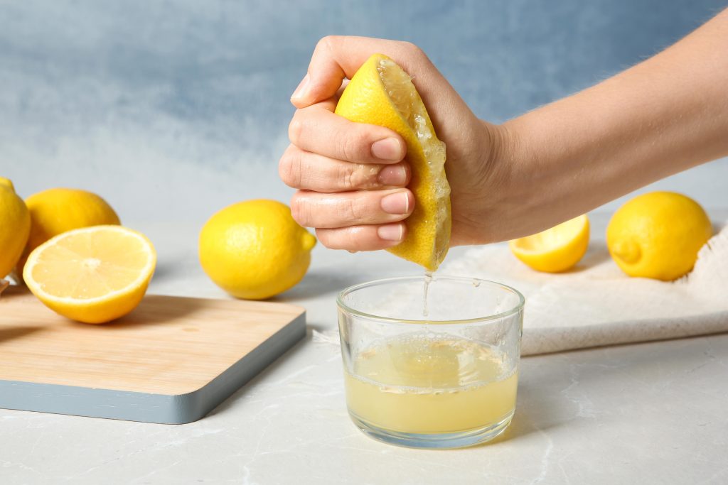 hand squeezing lemon juice into a cup from half cut lemon on a counter with cutting board in the background