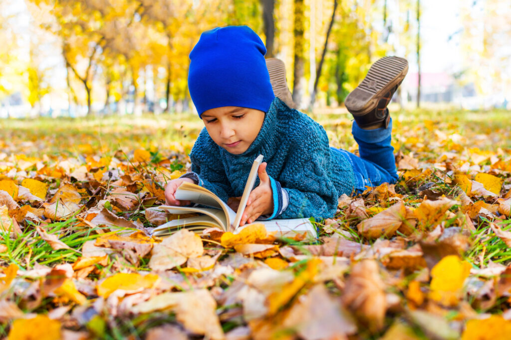 boy lying on his stomach reading a book in the fall in the Park